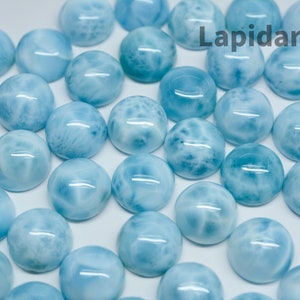 Könnte beinhalten: Eine Sammlung von hellblauen Cabochon-Edelsteinen mit einem weißen marmorierten Muster. Die Edelsteine sind in einem zufälligen Muster auf einer weißen Oberfläche angeordnet. Der Text "Lapidarians" ist in der oberen rechten Ecke des Bildes sichtbar.