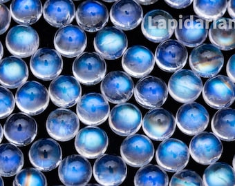Op de afbeelding: Een close-up van een verzameling ronde, iriserende maansteen cabochons. De stenen zijn melkachtig wit met een blauwe schittering.