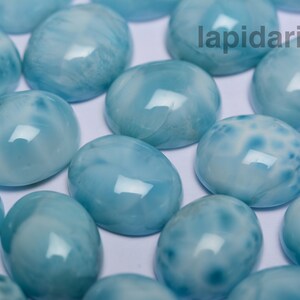 May include: A collection of oval-shaped, light blue cabochon gemstones with white marbling. The stones are smooth and polished, with a glossy finish.