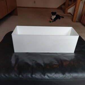 May include: A white rectangular planter on a black leather ottoman.