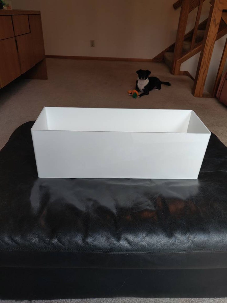 May include: A white rectangular planter on a black leather ottoman.