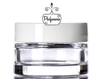 May include: A clear, round glass jar with a white lid. The jar has a layered design and reflects light. Above the jar is a black and white logo that says "The Parfumerie".