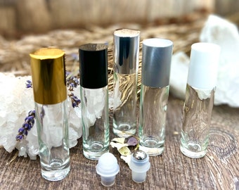 May include: Five clear glass roller bottles with different colored caps. The caps are gold, black, silver, gray, and white. The bottles are sitting on a wooden surface.