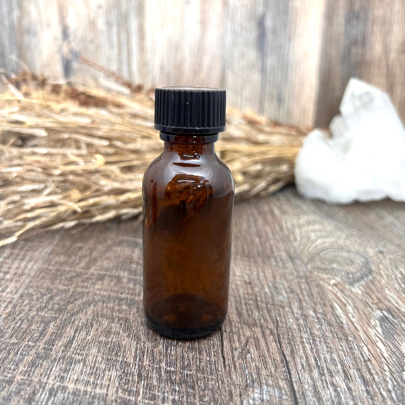 May include: A small amber glass bottle with a black screw-on lid. The bottle is sitting on a wooden surface.