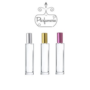Puede incluir: Tres botellas de perfume de vidrio con tapas de diferentes colores. Las botellas son transparentes y rectangulares. Las tapas son plateadas, doradas y rosadas.