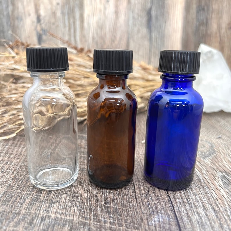 May include: Three glass bottles with black lids. The bottles are clear, amber, and blue.