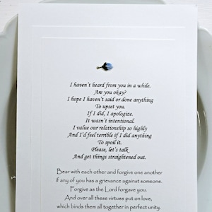 May include: A white card with a handwritten message about forgiveness and reconciliation. The message includes a quote from Colossians 3:13-14: "Bear with each other and forgive one another if any of you has a grievance against someone. Forgive as the Lord forgave you. And over all these virtues put on love, which binds them all together in perfect unity."