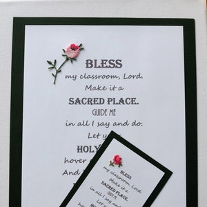May include: A white card with black text and a pink embroidered flower. The text reads "Bless my classroom, Lord. Make it a Sacred Place. Guide me in all I say and do. Let your Holy Spirit hover over all of us. And keep us in your Loving Care."