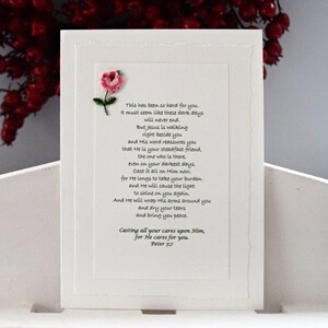 May include: A white card with a pink embroidered flower in the top left corner. The card features a poem about finding strength and comfort in faith. The poem includes the text "This has been so hard for you. It must seem like these dark days will never end. But Jesus is walking right beside you and His word reassures you that He is your steadfast friend, the one who is there, even on your darkest days. Cast it all on Him now, for He longs to take your burden, and He will cause the light to shine on you again. And He will wrap His arms around you and dry your tears and bring you peace. Casting all your cares upon Him, for He cares for you. Peter 5:7"