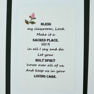 May include: A white card with black text and a pink flower in the top left corner. The text reads: "BLESS my classroom, Lord. Make it a SACRED PLACE. GUIDE ME in all I say and do. Let your HOLY SPIRIT hover over all of us. And keep us in your LOVING CARE."