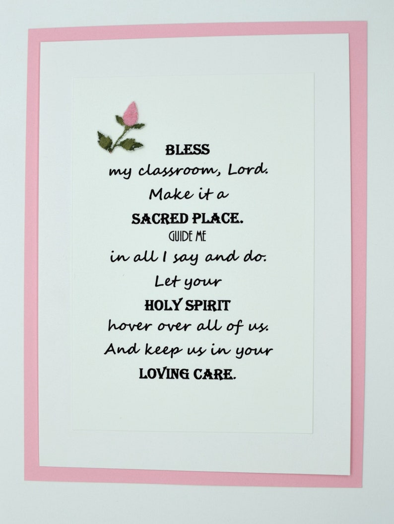 May include: A white card with a pink border and a small pink flower in the top left corner. The card has a poem printed on it that reads: "BLESS my classroom, Lord. Make it a SACRED PLACE. GUIDE ME in all I say and do. Let your HOLY SPIRIT hover over all of us. And keep us in your LOVING CARE."
