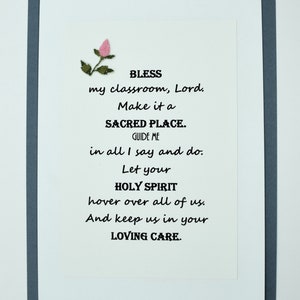 May include: A white card with a gray border and a pink flower in the top left corner. The card has a poem on it that reads: "BLESS my classroom, Lord. Make it a SACRED PLACE. GUIDE ME in all I say and do. Let your HOLY SPIRIT hover over all of us. And keep us in your LOVING CARE."