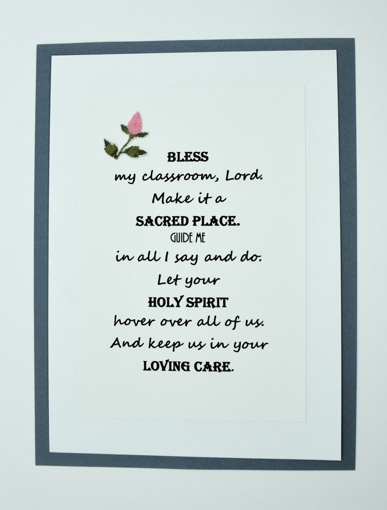 May include: A white card with a gray border and a pink flower in the top left corner. The card has a poem on it that reads: "BLESS my classroom, Lord. Make it a SACRED PLACE. GUIDE ME in all I say and do. Let your HOLY SPIRIT hover over all of us. And keep us in your LOVING CARE."