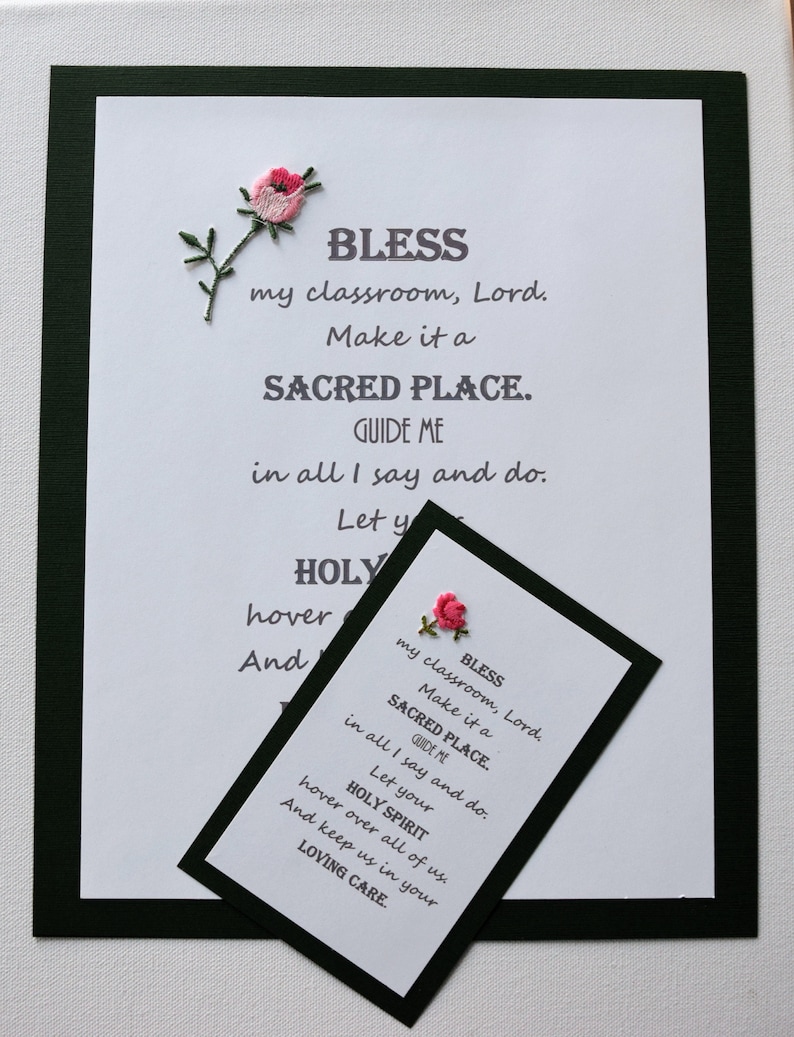 May include: A white card with black text and a pink embroidered flower. The text reads "Bless my classroom, Lord. Make it a Sacred Place. Guide me in all I say and do. Let your Holy Spirit hover over all of us. And keep us in your Loving Care."