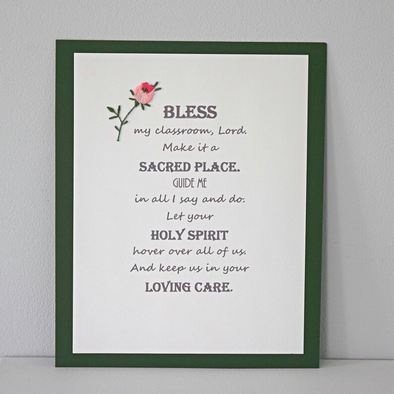 May include: A framed print with a green frame and a white background. The print features a poem about blessing a classroom, with the text "BLESS my classroom, Lord. Make it a SACRED PLACE. GUIDE ME in all I say and do. Let your HOLY SPIRIT hover over all of us. And keep us in your LOVING CARE."