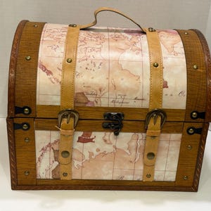 May include: A decorative wooden chest with a map design. The chest features a curved top and is trimmed with dark brown wood. Tan leather straps with brass buckles and a handle add to the vintage aesthetic. The chest is secured with a metal clasp.