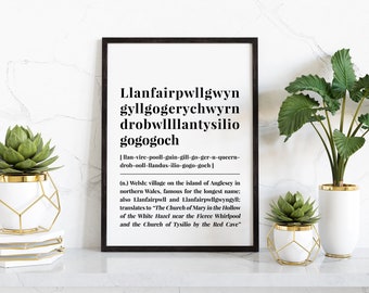 May include: A black framed print with white text that reads "Llanfairpwllgwyn gyllgogerychwyrn drobwllllantysilio gogogoch" and a phonetic pronunciation of the word. The print is hanging on a white wall with two potted plants in front of it.