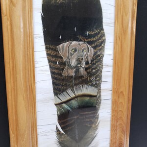 May include: A framed painting of a brown dog's head on a turkey feather. The feather is painted with brown, black, and white stripes. The dog's eyes are painted with white highlights. The painting is signed "CH 2013" in the bottom right corner.