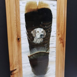 May include: A framed painting of a white dog with brown spots, looking directly at the viewer. The dog is painted on a brown and black feather with a white background. The painting is signed "C.H. 2018".