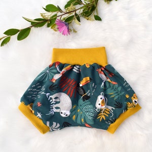 Peut inclure: Short de bain pour enfant en vert et jaune avec un imprimé d'animaux de la jungle. L'imprimé représente des toucans, des paresseux, des singes et des perroquets.
