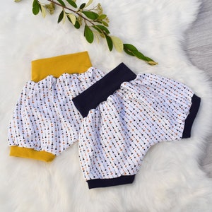 Peut inclure: Deux paires de bloomers pour tout-petits avec un fond blanc et un motif de petits triangles colorés. Une paire a une ceinture jaune et l'autre une ceinture bleu marine.