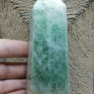May include: A large, green fluorite crystal point with a light green and white color pattern. The crystal is polished and has a smooth, glassy surface.