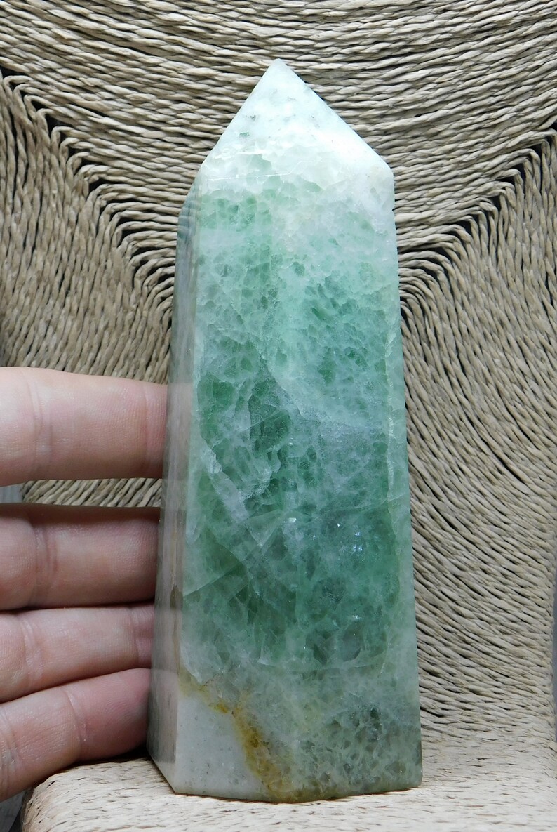 May include: A large, green fluorite crystal point with a light green and white color pattern. The crystal is polished and has a smooth, glassy surface.
