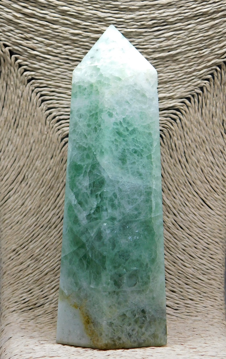 May include: A green fluorite crystal point with a white and green color pattern. The crystal is polished and has a smooth surface.