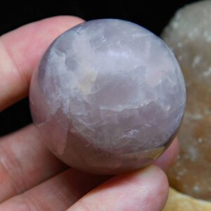 May include: A smooth, pale lavender amethyst sphere with a cloudy, translucent appearance. The sphere is approximately 2 inches in diameter.