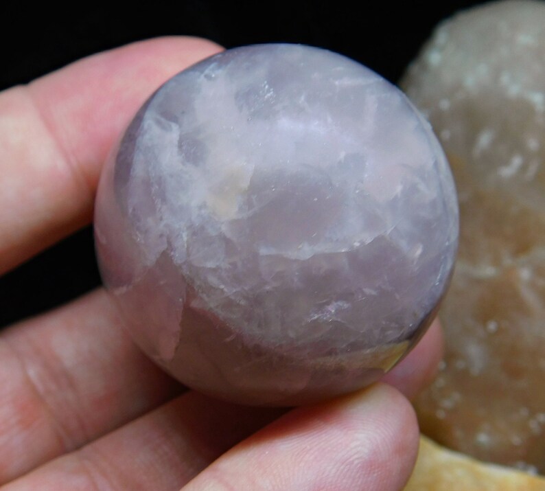 May include: A smooth, pale lavender amethyst sphere with a cloudy, translucent appearance. The sphere is approximately 2 inches in diameter.