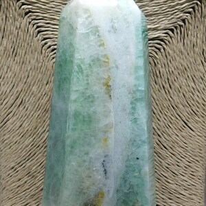 May include: A green and white crystal point, also known as a crystal wand, with a pointed tip and a flat base. The crystal has a natural, raw look with visible inclusions and striations.