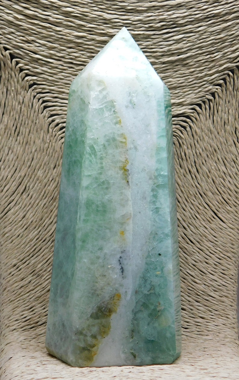 May include: A green and white crystal point, also known as a crystal wand, with a pointed tip and a flat base. The crystal has a natural, raw look with visible inclusions and striations.