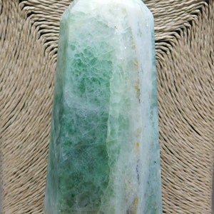 May include: A green and white fluorite crystal point, also known as a crystal wand, with a smooth, polished surface. The crystal is a natural stone with a unique, layered pattern.