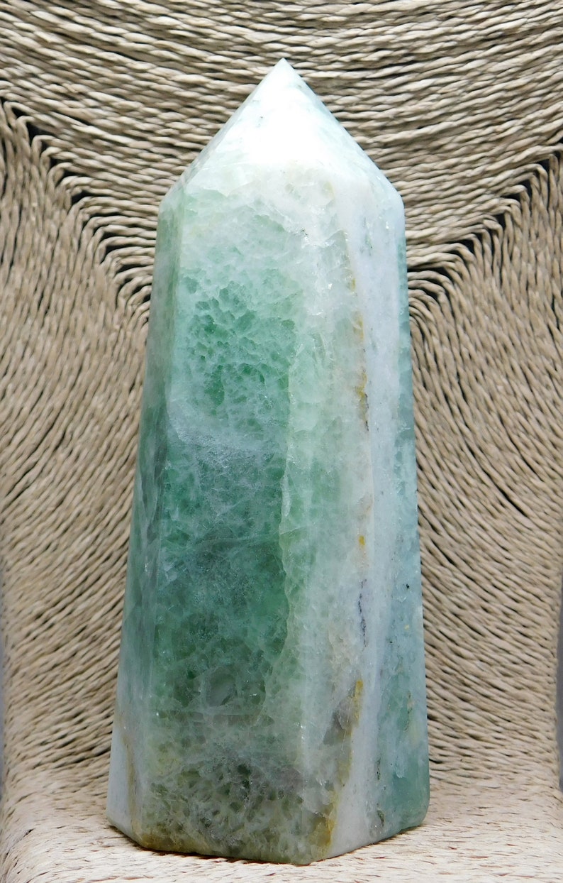 May include: A green and white fluorite crystal point, also known as a crystal wand, with a smooth, polished surface. The crystal is a natural stone with a unique, layered pattern.