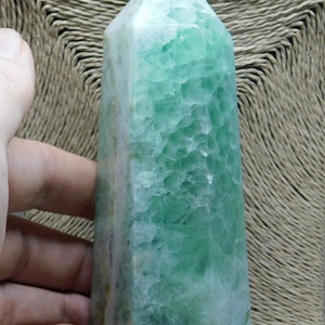 May include: A green fluorite crystal point with a white base. The crystal is polished and has a smooth, glassy surface.