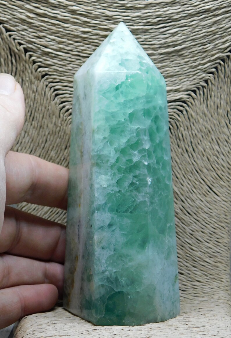 May include: A green fluorite crystal point with a white base. The crystal is polished and has a smooth, glassy surface.
