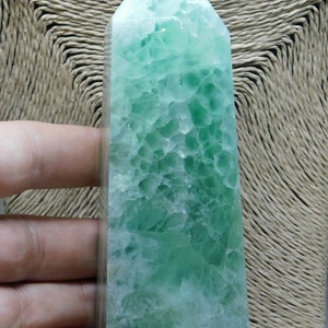 May include: A green fluorite crystal point, also known as a wand, with a light green and white color pattern. The crystal is polished and has a smooth, glassy surface.
