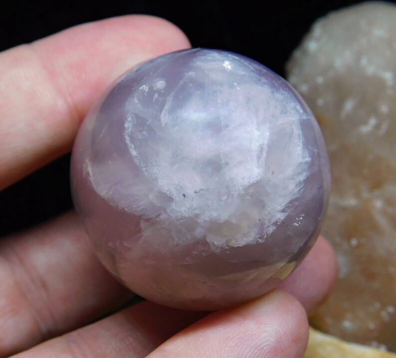 May include: A smooth, polished, lavender fluorite sphere with a white, cloudy interior. The sphere is approximately 2 inches in diameter.