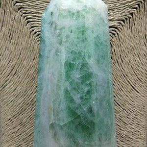 May include: A green and white crystal point, also known as a crystal wand, with a pointed tip and a hexagonal base. The crystal is translucent and has a natural, rough texture.