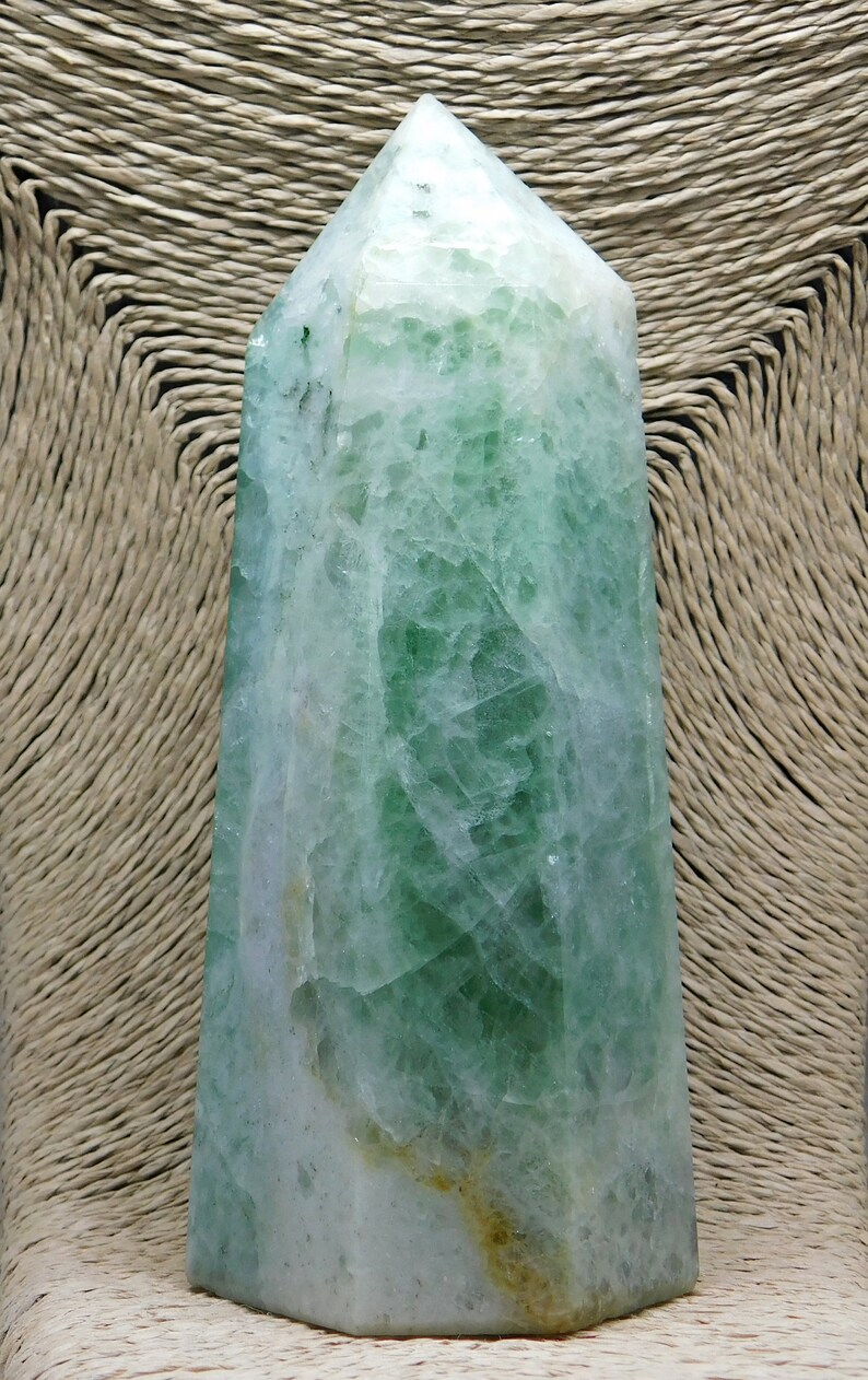 May include: A green and white crystal point, also known as a crystal wand, with a pointed tip and a hexagonal base. The crystal is translucent and has a natural, rough texture.