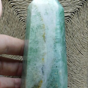 May include: A green and white fluorite crystal point, also known as a wand, with a natural, raw finish. The crystal is translucent and has a striated pattern.