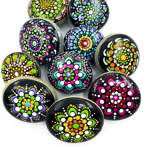 May include: A set of ten painted rocks featuring mandala designs. The rocks are black with colourful dots and patterns. The designs include flowers, swirls, and geometric shapes.