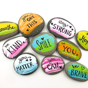 May include: Painted rocks with positive messages, including "you got this", "be kind", "smile", "stay strong", "have hope", "you matter", "you can", and "be brave".