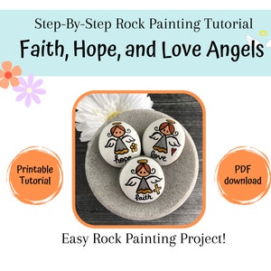 May include: Three painted rocks with angel designs. Each rock has a different word painted on it: "faith", "hope", and "love".