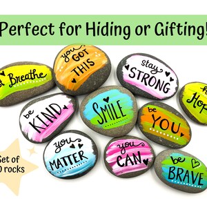 May include: Set of ten painted rocks with positive messages, including "just breathe", "you got this", "stay strong", "be kind", "smile", "be you", "you matter", "you can", "have hope", and "be brave".
