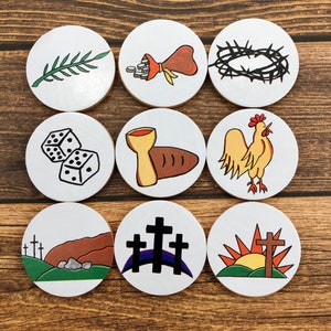 May include: Nine white circular game pieces with black outlines, each depicting a different scene from the story of Jesus Christ. The scenes include a palm branch, a bag of coins, a crown of thorns, two dice, a chalice and bread, a rooster, three crosses on a hill, three crosses with a rainbow, and a cross with a sunrise.