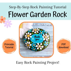 May include: A painted rock with a flower garden design. The rock is painted black with white and blue daisies. The center of the rock has a blue oval with the words "thank you" in white.