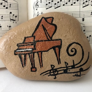 May include: A hand-painted rock with a brown grand piano and musical notes on a beige background.