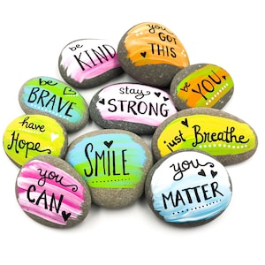 May include: Painted rocks with positive messages like "be kind", "stay strong", "you matter", and "just breathe".