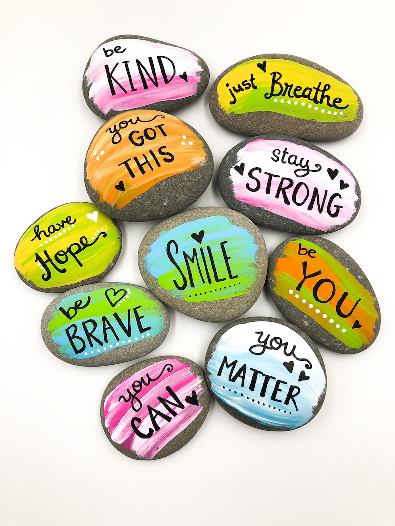 May include: Ten painted rocks with inspirational messages, including "be kind", "you got this", "just breathe", "stay strong", "have hope", "be brave", "smile", "be you", "you can", and "you matter".